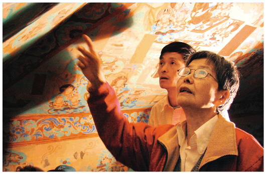 ▲樊錦詩（右一）在莫高窟第八十五窟壁畫修復現(xiàn)場。（敦煌研究院供圖）